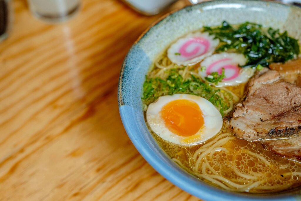 Fukuoka in April: Cherry Blossoms, Ramen, and Slow Spring Days (2026 Itinerary) Close-up of a savory Japanese ramen bowl featuring noodles, egg, and toppings on a wooden table.